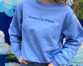May include: A light blue sweatshirt with the text "Protect Our Planet" and a small globe symbol embroidered on the front.