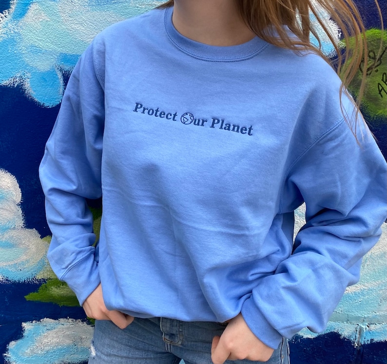 May include: A light blue sweatshirt with the text "Protect Our Planet" and a small globe symbol embroidered on the front.