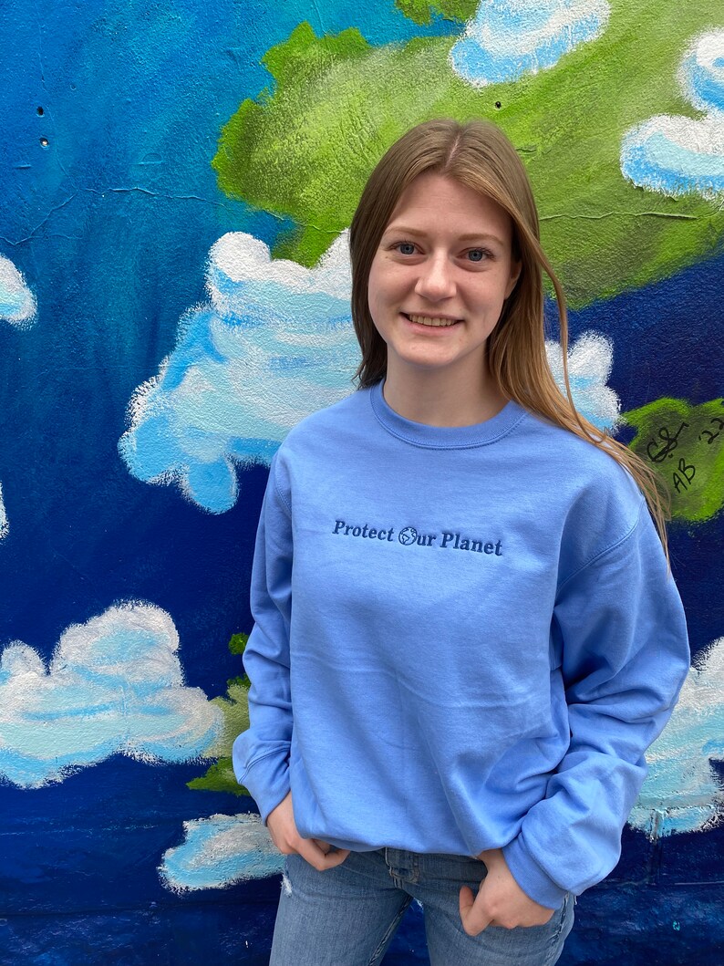 May include: A light blue long-sleeved sweatshirt with the text "Protect Our Planet" and a small globe icon embroidered on the front.