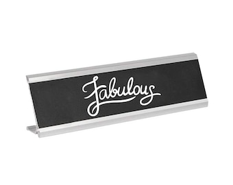 May include: A silver desk nameplate with a black surface and the word "fabulous" written in white cursive.