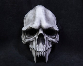 May include: A white skull mask with sharp teeth and a black strap. The mask is made of a hard material and has a realistic look.