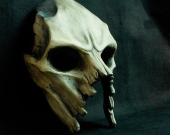 May include: A detailed, off-white skull mask with a cracked and weathered appearance. The mask has a large, open mouth and a long, pointed nose.
