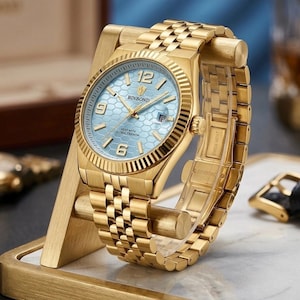 May include: A gold-tone wristwatch with a light blue dial featuring a hexagonal honeycomb pattern. The watch has a fluted bezel, gold-tone hands, and gold-tone hour markers with the numbers 12, 6, and 9. The text BINBOND is printed on the dial.