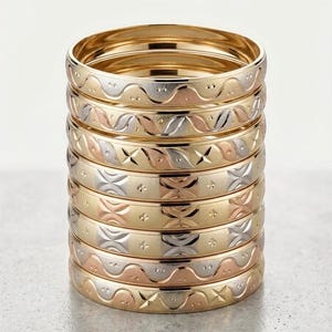 May include: A stack of eight circular bangles featuring a tri-color metal design in yellow, rose, and white tones. Each bangle displays distinct engraved patterns including wavy lines, repeating leaf-like motifs, and small star-shaped accents.
