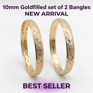 May include: A set of two gold-filled bangles with a 10mm width, featuring textured surfaces with engraved star and chevron patterns. The text 10mm Goldfilled set of 2 Bangles, NEW ARRIVAL, and BEST SELLER is displayed in the image.