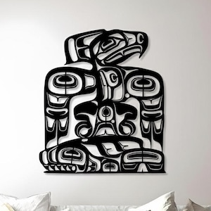 May include: A black, stylized metal wall art piece depicting a Native American totem design. The artwork features a detailed, symmetrical design with a bird at the top and other symbolic shapes. The piece is mounted on a white wall above a sofa.