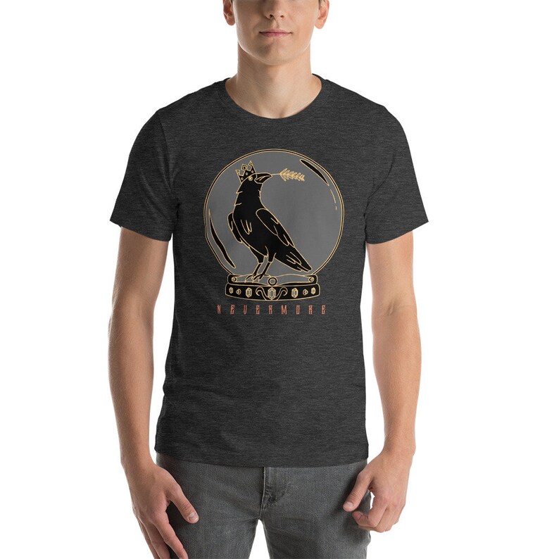 May include: A dark heather grey t-shirt with a graphic of a crow wearing a crown inside a glass sphere. The crow is holding a branch in its beak. The text "NEVERMORE" is printed below the sphere.
