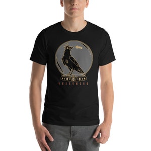 May include: Black t-shirt with a graphic of a crow wearing a crown and holding a branch in its beak. The crow is inside a circle with a gray background. The text "NEVERMORE" is printed below the circle.
