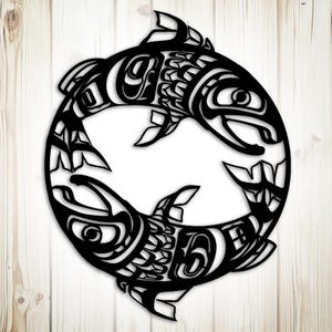 May include: Black metal art piece featuring two stylized fish in a circular design. The fish are intricately detailed with curved lines and shapes, creating a symmetrical and balanced composition. The artwork is set against a light wood background.