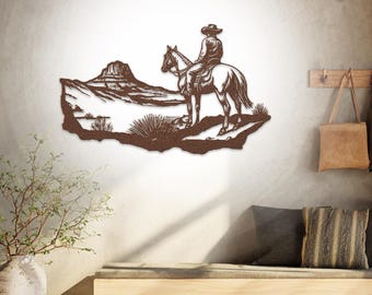 May include: A brown metal wall art piece depicting a cowboy on horseback in a desert landscape. The artwork features a cowboy wearing a hat and riding a horse, with a mountain and desert plants in the background. The art is mounted on a light-colored wall.