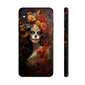 May include: A black phone case featuring a Day of the Dead design. The artwork depicts a woman with sugar skull makeup, surrounded by autumn leaves and flowers in shades of orange, red, and gold. The case has a glossy finish.
