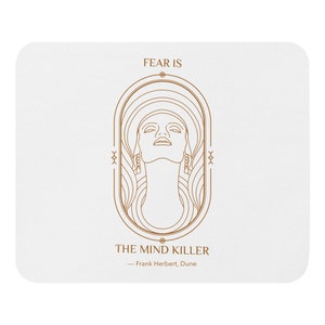 May include: White mousepad with a brown line art design featuring a woman's face and the text "FEAR IS THE MIND KILLER - Frank Herbert, Dune". The design is in a vertical oval shape.