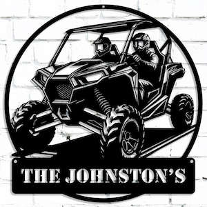 May include: Black and white silhouette of a side-by-side off-road vehicle with two people driving. The vehicle is in a circular frame with the text "THE JOHNSTON'S" below.