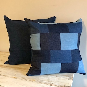 May include: Two decorative throw pillows with a patchwork design. One pillow is made of solid dark blue denim, while the other is made of various shades of blue denim sewn together in a grid pattern.