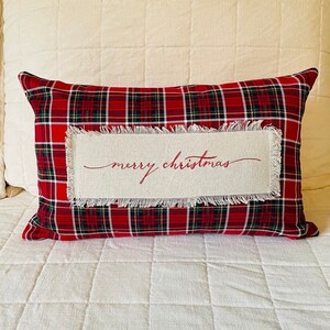 May include: Red and green plaid throw pillow with a white fabric insert that says "merry christmas" in red cursive.