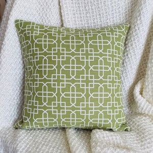May include: A green throw pillow with a white geometric pattern. The pillow is sitting on a white textured blanket.