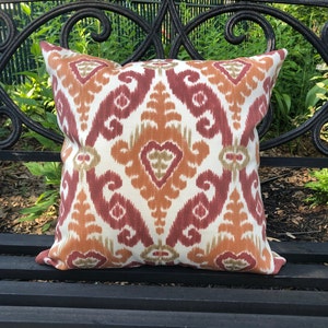 May include: A decorative throw pillow with an orange, red, and white ikat pattern. The pillow is sitting on a black metal bench.
