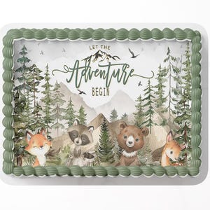 May include: A rectangular cake with a green border and a forest-themed design. The image features a mountain scene with trees, birds, and woodland animals, including a fox, raccoon, bear, and deer. The text "Let the Adventure Begin" is displayed.