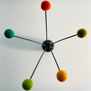 Könnte beinhalten: Eine schwarze Vase mit fünf Stielen, die farbige Filzkugeln halten. Die Kugeln sind orange, grün und gelb.