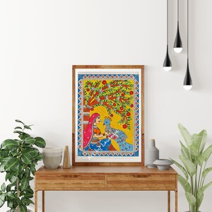 May include: A framed painting of a woman in a colorful sari sitting under a tree with a peacock. The painting is done in a folk art style with bright colors and simple lines.