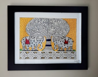 May include: Framed artwork featuring two gray elephants flanking a tree with a white and black leaf design. The background is yellow with a textured pattern. The elephants have red and black accents. The artwork is in a black frame.