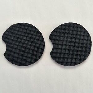 May include: Two black round cup coasters with a cut-out for a handle. The coasters have a textured surface.