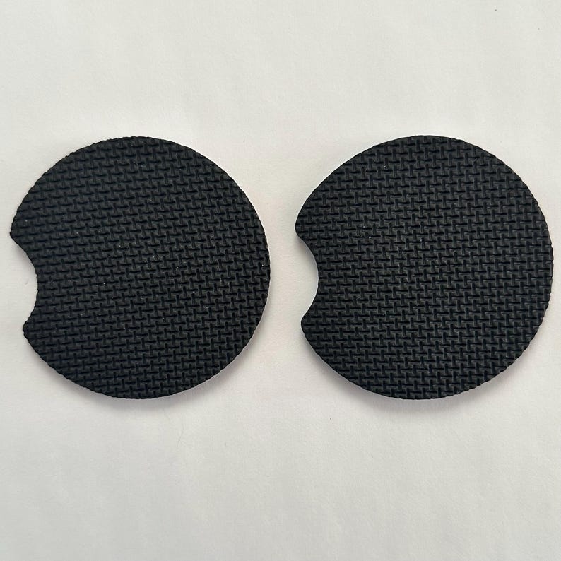 May include: Two black round cup coasters with a cut-out for a handle. The coasters have a textured surface.