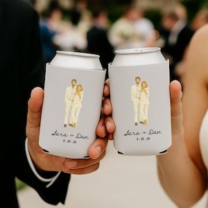 May include: Two gray can coolers, each featuring a couple illustration and the text "Sara + Dan 9.25.26". The coolers are held up, likely at a wedding or celebration. The design is simple and elegant.