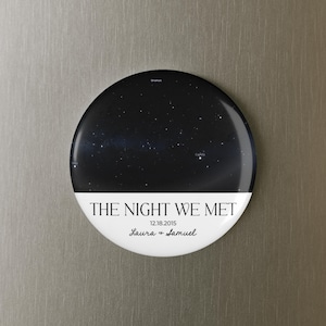 May include: A circular magnet with a night sky design. The top half shows a dark blue background with white stars. The bottom half is white with the text "THE NIGHT WE MET", date, and names. A decorative item.