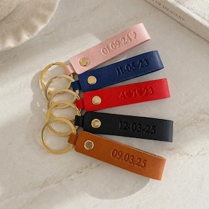 Può includere: Cinque portachiavi in pelle rosa, blu navy, rosso, nero e marrone. Ogni portachiavi ha un anello color oro e un cinturino con date impresse: 01.09.24, 11.05.23, 4.07.23, 12.03.25 e 09.03.25. Ogni cinturino ha un rivetto color oro.