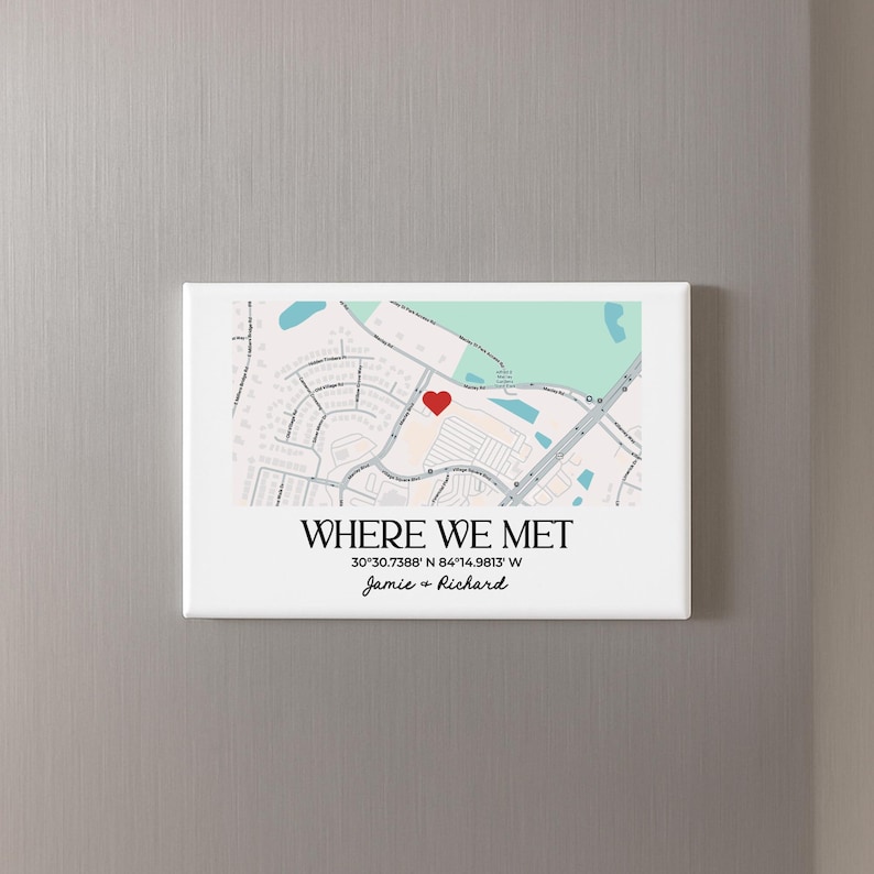 May include: A white rectangular magnet with a map design. The map features a red heart marking a location, with the text "WHERE WE MET" and the coordinates 30&deg;30.7388' N 84&deg;14.9813' W. The names "Jamie & Richard" are also included.