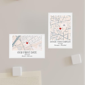 May include: Two rectangular white magnets with map designs. One magnet reads "OUR FIRST DATE" with a date and names. The other says "DONDE TODO EMPEZO" with a date and names. Both feature a red heart marking a location on the map.