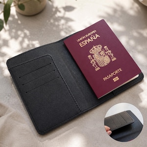 Peut inclure: Un porte-passeport noir avec trois fentes pour cartes, contenant un passeport espagnol bordeaux. Le passeport porte l'inscription dor&eacute;e "UNION EUROPEA ESPA&Ntilde;A PASAPORTE". Le porte-passeport est ouvert, r&eacute;v&eacute;lant le passeport et les fentes int&eacute;rieures.