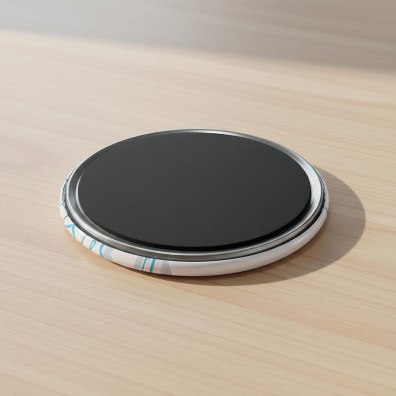 May include: A round magnet with a black center and a white and blue patterned border. The magnet is sitting on a light brown wooden surface.