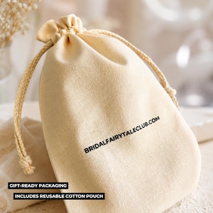 Peut inclure: Pochette en coton beige avec cordon de serrage, portant l'inscription noire "BRIDALFAIRYTAILCLUB.COM". Le sac est nou&eacute; avec une corde beige et porte les mentions "EMBALLAGE CADEAU" et "COMPREND UNE POCHETTE EN COTON R&Eacute;UTILISABLE".