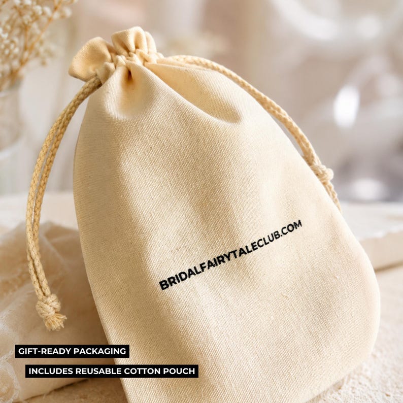 Peut inclure: Pochette en coton beige avec cordon de serrage, portant l'inscription noire "BRIDALFAIRYTAILCLUB.COM". Le sac est nou&eacute; avec une corde beige et porte les mentions "EMBALLAGE CADEAU" et "COMPREND UNE POCHETTE EN COTON R&Eacute;UTILISABLE".