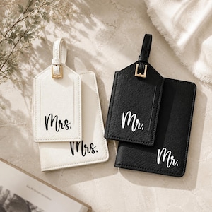 Puede incluir: Un juego de etiqueta de equipaje y portapasaporte blanco con el texto Mrs. en negro, junto a un juego negro con el texto Mr. en blanco. Ambos conjuntos presentan un acabado texturizado, hebillas en tono dorado y correas a juego.