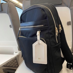 Peut inclure: Sac &agrave; dos noir en nylon avec fermetures &eacute;clair et d&eacute;tails dor&eacute;s. Comprend une &eacute;tiquette de bagage cr&egrave;me avec les initiales "RL". Le sac &agrave; dos a plusieurs compartiments et un dos rembourr&eacute;, id&eacute;al pour les voyages ou l'usage quotidien.