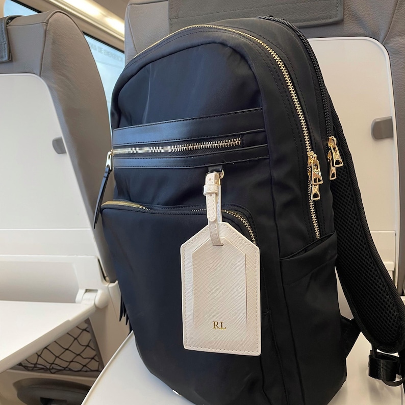 Peut inclure: Sac &agrave; dos noir en nylon avec fermetures &eacute;clair et d&eacute;tails dor&eacute;s. Comprend une &eacute;tiquette de bagage cr&egrave;me avec les initiales "RL". Le sac &agrave; dos a plusieurs compartiments et un dos rembourr&eacute;, id&eacute;al pour les voyages ou l'usage quotidien.