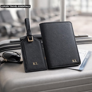 Peut inclure: Ensemble d'accessoires de voyage noirs, comprenant un porte-passeport et une &eacute;tiquette de bagage, tous deux avec les initiales dor&eacute;es "KL". L'&eacute;tiquette a une sangle et une boucle. Le texte "LUXURY TRAVEL ESSENTIALS" est en haut.
