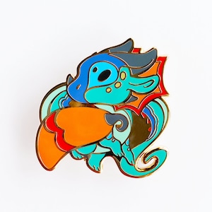 May include: A colourful enamel pin featuring a blue, green and orange dragon with a red and gold wing. The dragon is curled up with its head tucked under its wing.