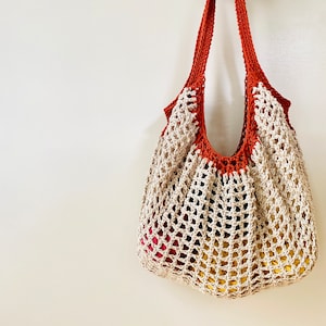 May include: A crocheted tote bag with a brown top and a beige bottom. The bag is hanging on a white wall.