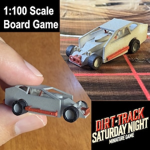 Op de afbeelding: Een miniatuur raceauto op schaal 1:100 voor een bordspel. De auto is grijs met zwarte wielen en oranje zijpanelen en voorbumper. De tekst in de afbeelding luidt 1:100 Scale Board Game en DIRT TRACK SATURDAY NIGHT MINIATURE GAME.