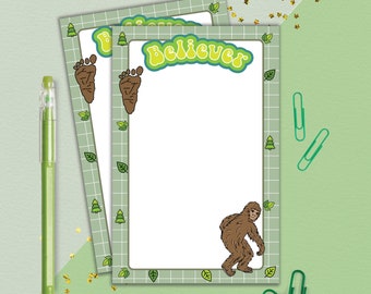 May include: Three green and white notepad pages with a green grid pattern and a brown footprint design. The top page has the word "Believer" in green letters. The bottom page has a brown cartoon Bigfoot.