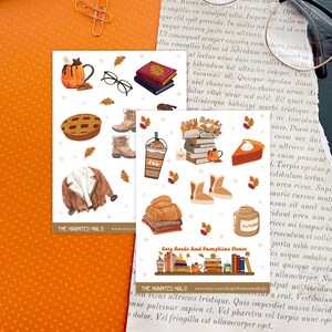 May include: A set of 16 autumn-themed stickers featuring illustrations of cozy sweaters, boots, mugs, books, pumpkins, and pies. The stickers are printed on white glossy paper with a gold glitter background. The text "Cozy Reads and Pumpkins Please" and "The Haunted Halo" are included on the stickers.