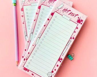 May include: Three rectangular notepads with a light pink background, featuring the text HIT LIST at the top. The design includes illustrations of knives, a mace, and red paint splatters. Each notepad has a checklist with dotted lines and circles.