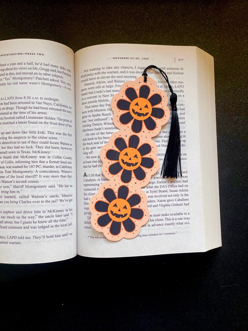 May include: Three orange and black Halloween-themed bookmarks with a jack-o-lantern face in the centre of each bookmark. The bookmarks are shaped like a flower with six petals.
