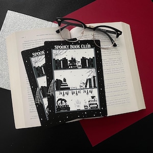 May include: Three black and white illustrated cards with the text "Spooky Book Club" on the front. The cards feature a bookshelf with books, a skull, a cauldron, and other spooky items.