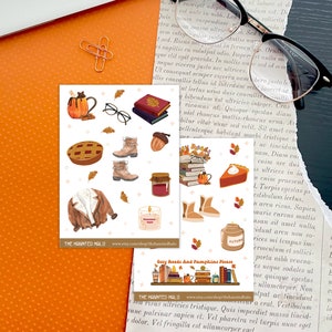 May include: A set of 12 autumn-themed stickers featuring illustrations of books, glasses, a mug of hot cocoa, a pie, a jacket, a candle, a jar of jam, boots, and acorns. The stickers are on a white background with the text "Cozy Reads And Pumpkins Please" and "The Haunted Halo" on the bottom.