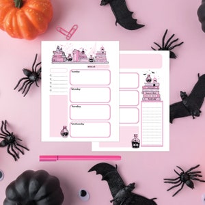 May include: A pink weekly planner with a witchy theme. The top of the planner features a stack of books with potion bottles and a spider web. The planner has sections for each day of the week, Sunday through Wednesday. The planner also has a section for notes.